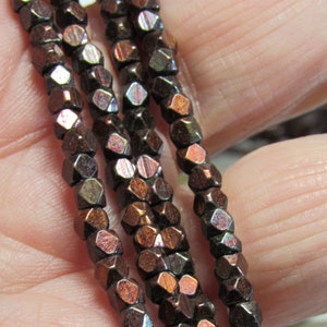 May include: A strand of dark brown metallic beads with a iridescent finish. The beads are faceted and have a hexagonal shape.