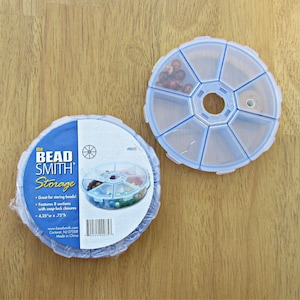 May include: A clear plastic bead storage container with eight sections. The container is open and shows beads in some of the sections. The container is labeled "the Bead Smith Storage" and has the text "Great for storing beads! Features 8 sections with snap-lock closures 4.25" x .75" www.beadsmith.com Corteret, NJ 07008 Made in China PB425".