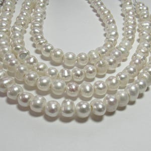 May include: A multi-strand necklace featuring lustrous white freshwater pearls. The pearls are irregularly shaped with a smooth, reflective surface, strung together on a clear cord. The strands are arranged in a cascading, layered formation.