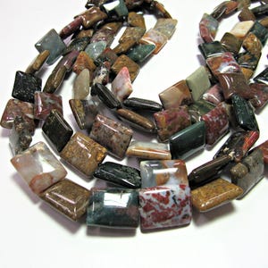 May include: A strand of colorful, rectangular, polished gemstone beads. The beads are a mix of brown, red, green, and white.