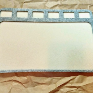 May include: A gray felt craft mat with a white surface and multiple cut-out rectangular shapes along the top edge.