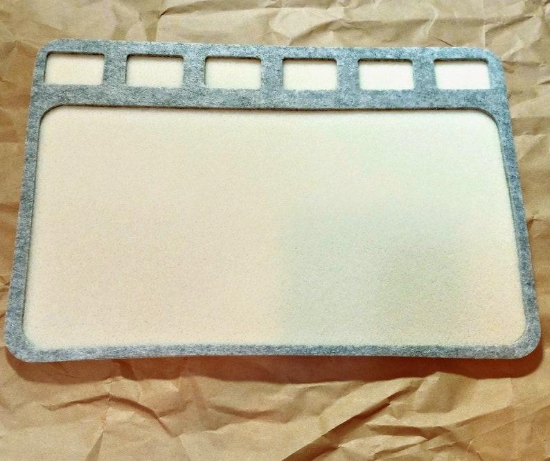 May include: A gray felt craft mat with a white surface and multiple cut-out rectangular shapes along the top edge.