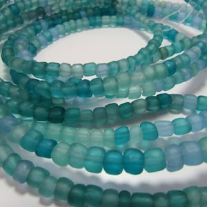 May include: A strand of teal blue and light blue glass beads. The beads are small and have a frosted finish.