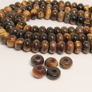May include: A strand of brown and gold tiger's eye beads with a golden sheen. There are also several loose tiger's eye beads in the image.
