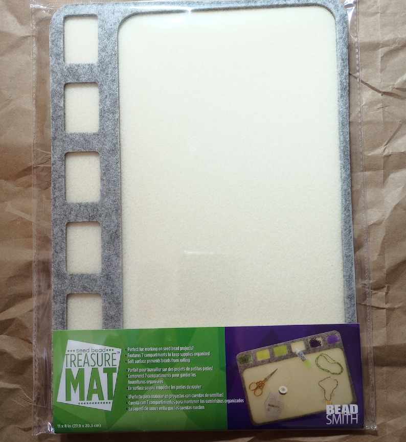 May include: Gray felt beading mat with seven compartments and a white felt surface. The mat is labeled "seed bead TREASURE MAT" and measures 11 x 8.5 inches (27.9 x 20.3 cm).
