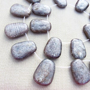 May include: A strand of silver and gray gemstone beads, each bead is a smooth, irregular oval shape.