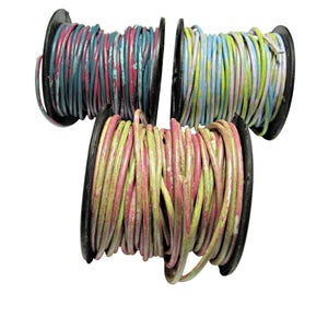 May include: Three spools of colorful leather cord. The cords are wrapped around black spools. The colors include teal, pink, yellow, and blue. The leather has a distressed, vintage appearance.