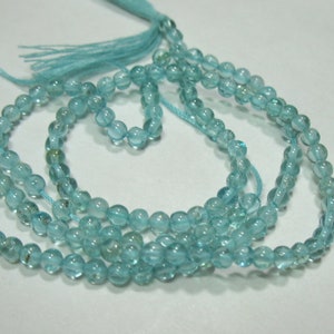 May include: A strand of light blue aquamarine beads, strung on a thin thread with a matching light blue tassel. The beads are round and slightly faceted, creating a subtle sparkle.