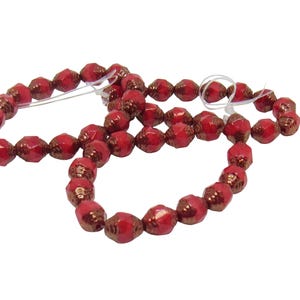 May include: A strand of red glass beads with a metallic copper finish. The beads are faceted and have a slightly irregular shape.