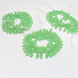 May include: Three strands of light green glass beads, each strung in a circle, with a white string connecting them.