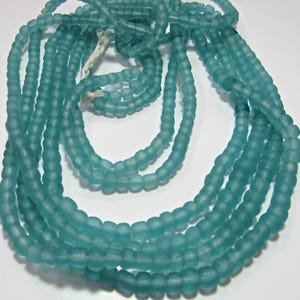 May include: A strand of turquoise blue glass beads. The beads are opaque and have a slightly frosted finish. The beads are strung on a white thread.