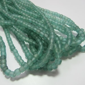 May include: A strand of light blue glass beads. The beads are small and round, and they have a frosted finish.