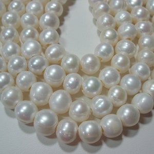 May include: A strand of round, off-white freshwater pearls with a lustrous, iridescent finish. Each pearl features a central hole for stringing, showcasing a smooth, organic surface texture with subtle variations in shape and size across the strand.
