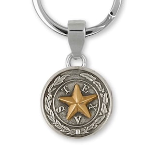 May include: Silver key chain with a round charm featuring the state seal of Texas. The charm has a gold five-pointed star in the center surrounded by a laurel wreath and the word "TEXAS" in a circle.