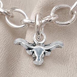 May include: A silver-toned charm shaped like a longhorn steer head, featuring prominent curved horns and a detailed snout. The charm is attached to a circular link of a silver-toned chain. The text Chain Sold Separately is visible at the bottom.