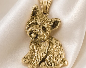 Puede incluir: Un colgante de tono dorado con forma de perro pequeño sentado, con detalles de pelaje texturizado y una oreja puntiaguda. El colgante cuenta con una anilla triangular en la parte superior para su sujeción. El texto "Chain sold separately." aparece abajo.