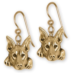 May include: Gold-toned dangle earrings featuring a detailed dog head design. The dog is looking to the side with its ears perked up.