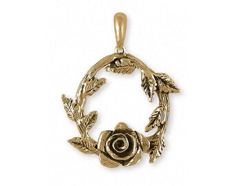 May include: Gold-toned pendant featuring a rose with leaves forming a circle. The rose is in the center of the circle and the leaves are arranged around it.