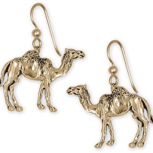 May include: A pair of gold-colored camel earrings. Each earring features a detailed, three-dimensional camel pendant suspended from a simple hook. The camels are depicted in a standing pose, with intricate detailing.