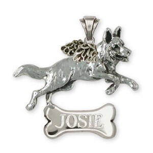 May include: A silver-colored pendant featuring a German Shepherd dog with angel wings, leaping forward. Below the dog is a bone-shaped tag with the name "JOSIE" engraved. The pendant is designed to be worn as a necklace.