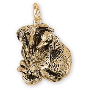 以下が含まれることがあります： 2匹の犬、おそらくアフガンハウンドの形をした金色のペンダント。ペンダントは、一緒に丸まっています。ペンダントは、チェーン用の小さなループが付いたテクスチャ加工された表面を持っています。犬は毛皮と顔の特徴で詳細に描かれています。