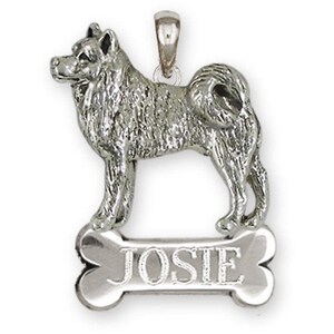 May include: A silver-colored pendant in the shape of a dog standing on a bone-shaped tag. The tag is engraved with the name "JOSIE". The pendant has a loop at the top for a chain.