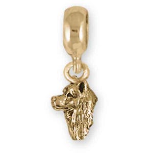 May include: A gold-colored charm featuring a detailed dog head pendant. The charm has a loop at the top for attaching to a bracelet or necklace. The dog's features are clearly defined, showcasing its fur and facial structure.