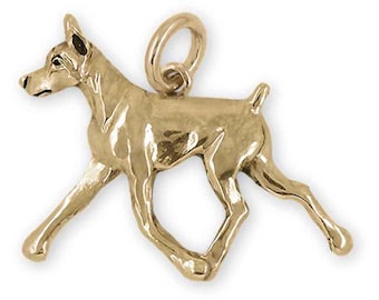 May include: A gold-colored charm in the shape of a Doberman Pinscher dog. The dog is depicted in a running pose with its head turned to the side.