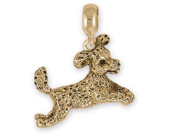May include: A gold-toned charm of a poodle dog jumping in the air. The charm is textured and has a detailed design.