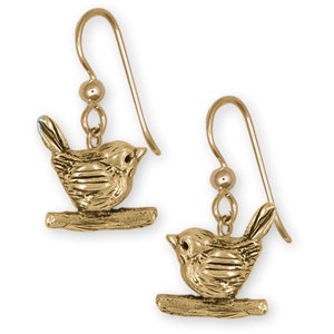May include: A pair of gold-colored bird earrings. Each earring features a small bird perched on a branch. The birds have detailed wings and bodies. The earrings have a hook closure.