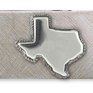 Puede incluir: Un clip para billetes plateado con un acabado cepillado. El clip presenta un contorno pulido en relieve del estado de Texas en el centro. El clip rectangular tiene un diseño simple y funcional.