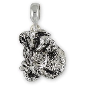 以下が含まれることがあります： 2匹のアフガンハウンドが寄り添う姿を描いたシルバーカラーのチャーム。ブレスレットやネックレスに取り付けるためのループが付いています。犬たちは毛並みが細かく表現されています。