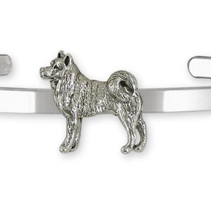 May include: A silver-toned cuff bracelet featuring a detailed Shiba Inu dog charm. The dog is standing, with its tail curled. The bracelet is a simple, open design, and the dog charm is the focal point.
