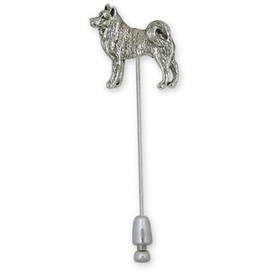 May include: A silver-colored Akita dog lapel pin. The pin features a detailed, three-dimensional sculpture of an Akita dog standing on a long, thin, silver-colored pin with a decorative end. The dog is facing left.