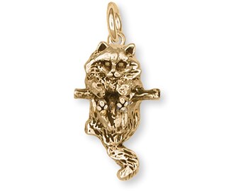 May include: A gold charm of a cat hanging from a branch. The cat is facing forward with its paws outstretched. The charm is detailed and realistic.