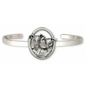 Puede incluir: Una pulsera de plata con un dije circular que presenta dos cabezas de galgos italianos. El dije es detallado y realista.