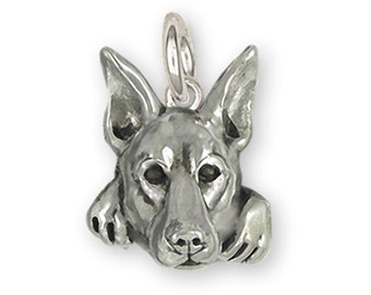 May include: Silver charm of a German Shepherd dog's head with paws on either side. The dog is looking forward with its tongue out.