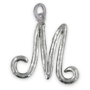 Può includere: Ciondolo in argento a forma della lettera M. La lettera è stilizzata con un carattere corsivo e ha una finitura testurizzata.