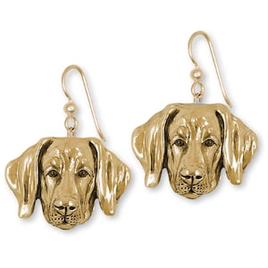 May include: A pair of gold-colored dog head earrings. The earrings feature a detailed, three-dimensional design of a dog's face, including the eyes, nose, and ears. The earrings hang from a simple hook.
