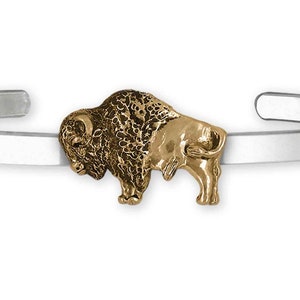 Può includere: Un braccialetto rigido in argento con un ciondolo a forma di bufalo dorato. Il bufalo è rivolto a sinistra e presenta un design dettagliato.