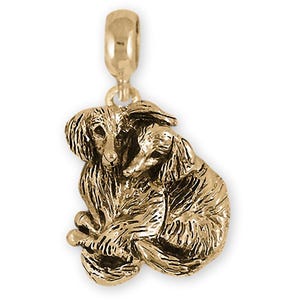 以下が含まれることがあります： 2匹の犬、おそらくアフガンハウンドが抱き合っている、金色のチャーム。ブレスレットやネックレスに取り付けるためのループが付いています。犬は毛並みが細かく表現され、質感が表現されています。ペンダントです。