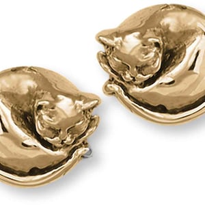 May include: A pair of gold-toned earrings featuring a sleeping cat design. The cat is curled up in a ball with its paws tucked under its chin.