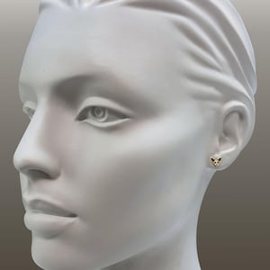 May include: A gold-colored stud earring with a cat-shaped design is worn on a white mannequin head. The earring has a black and gold pattern. The mannequin head is white and has a neutral background. The text "Design © Esquivel & Fees" is in the bottom left corner.