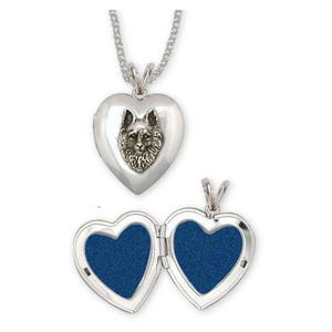 Puede incluir: Un collar con un dije en forma de corazón de plata, grabado con la cabeza de un perro en la parte delantera. El dije se abre para revelar un interior de terciopelo azul.