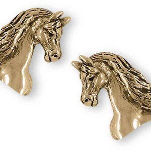 May include: Two gold-colored horse head-shaped earrings. The earrings are detailed with flowing manes and are set against a white background. The horse heads are facing opposite directions.