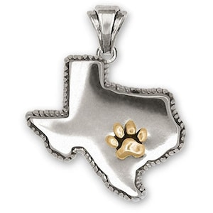 Puede incluir: Colgante de plata con forma del estado de Texas con una huella de pata dorada en el centro.