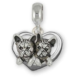以下が含まれることがあります： ハート型のフレームの中に2匹のフレンチブルドッグが描かれたシルバーチャーム。チャームの上部には、ブレスレットやネックレスに取り付けるためのループが付いています。犬たちは、質感のある毛並みと表情豊かな顔で詳細に表現されています。
