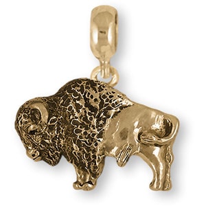 May include: A gold-colored charm in the shape of a bison. The charm has a detailed texture on the bison's body and a loop at the top for attaching to a bracelet or necklace. The bison is standing with its head slightly lowered.
