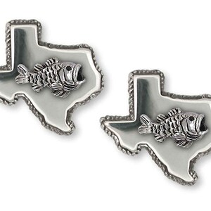Puede incluir: Un par de gemelos plateados. Cada gemelo tiene la forma del estado de Texas, con un pez detallado en el centro. Los bordes tienen un borde en forma de cuerda. Los gemelos están sobre un fondo blanco.