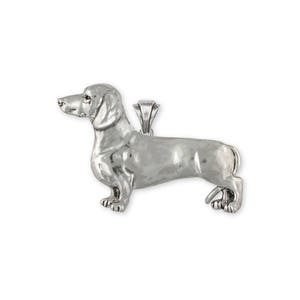 May include: A silver-toned metal pendant shaped like a dachshund dog in a standing profile position. The pendant features a smooth, reflective surface with detailed contours of the dog's head, long body, and short legs, including a small bail at the top.